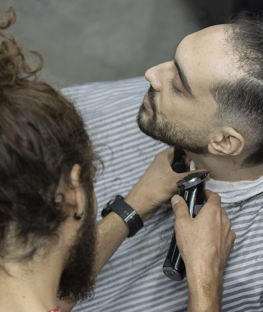 A barber trimming a beard with clippers